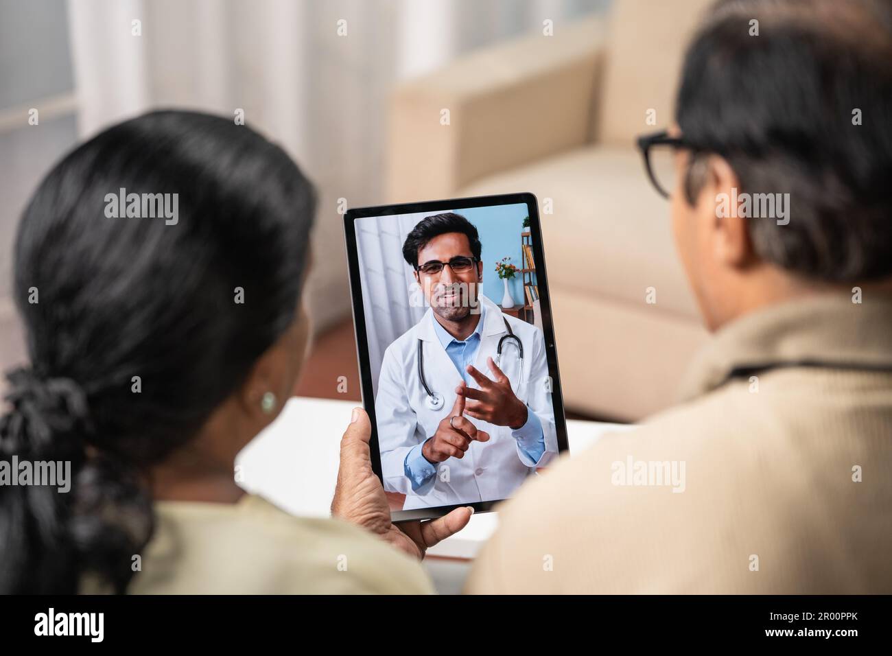 Spalla shot di coppia indiana anziano che prende consiglio dal medico durante la videochiamata online da scheda a casa - concetto di assistenza sanitaria remota, virtuale Foto Stock