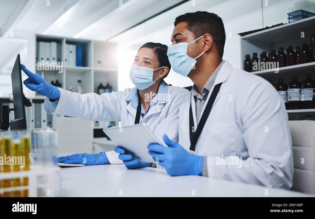 Il duro lavoro ci porterà la cura. due giovani ricercatori che utilizzano dispositivi digitali in un laboratorio. Foto Stock