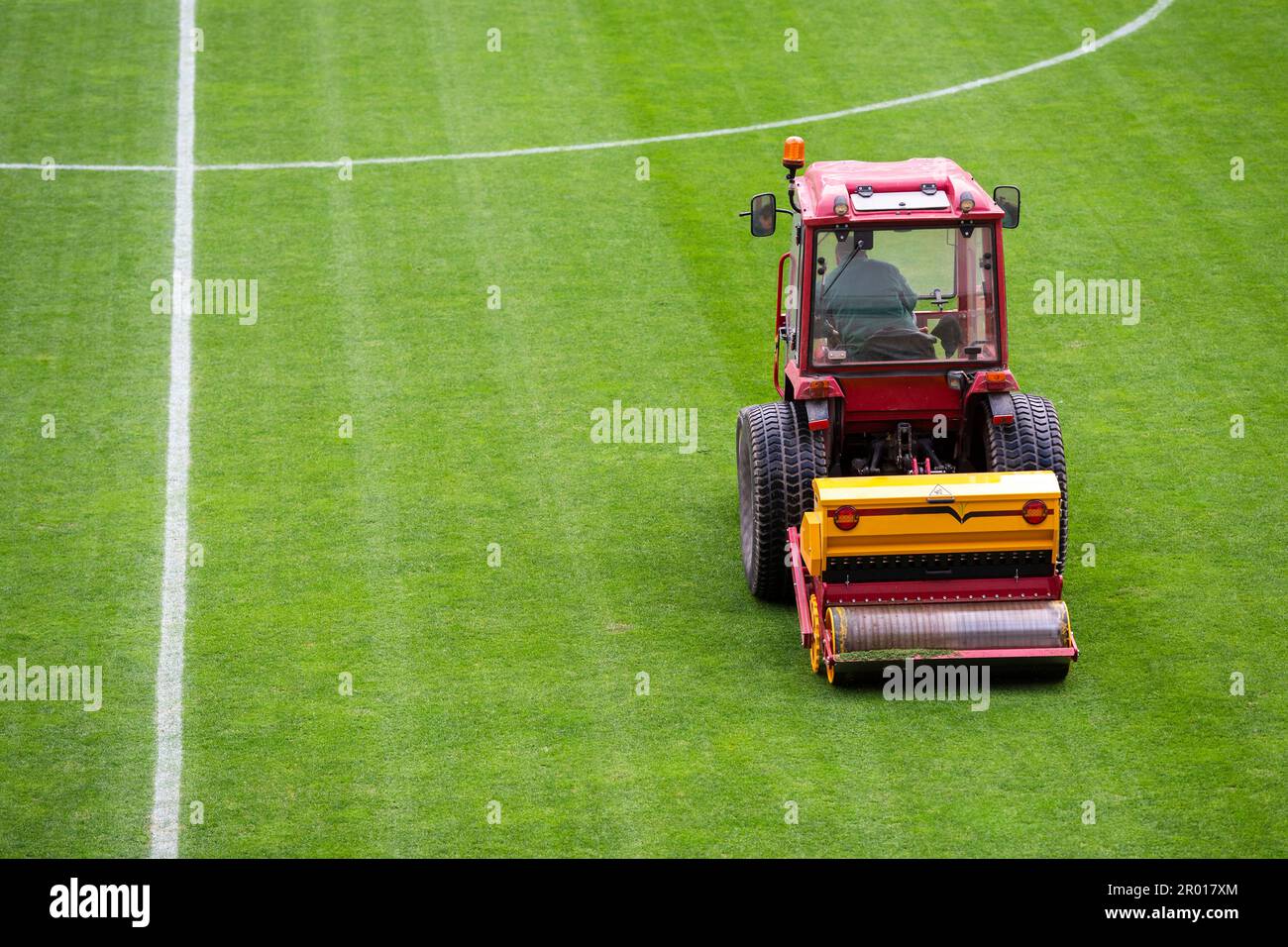 Un uomo su un trattore con una seminatrice a disco deve praticare l'erba di zenzero sul campo da calcio Foto Stock