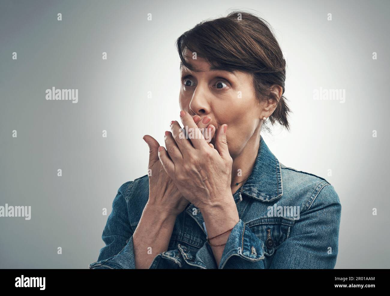 Ora è uno scandalo e mezzo. Studio shot di una donna anziana che copre la bocca e che guarda scioccato su uno sfondo grigio. Foto Stock