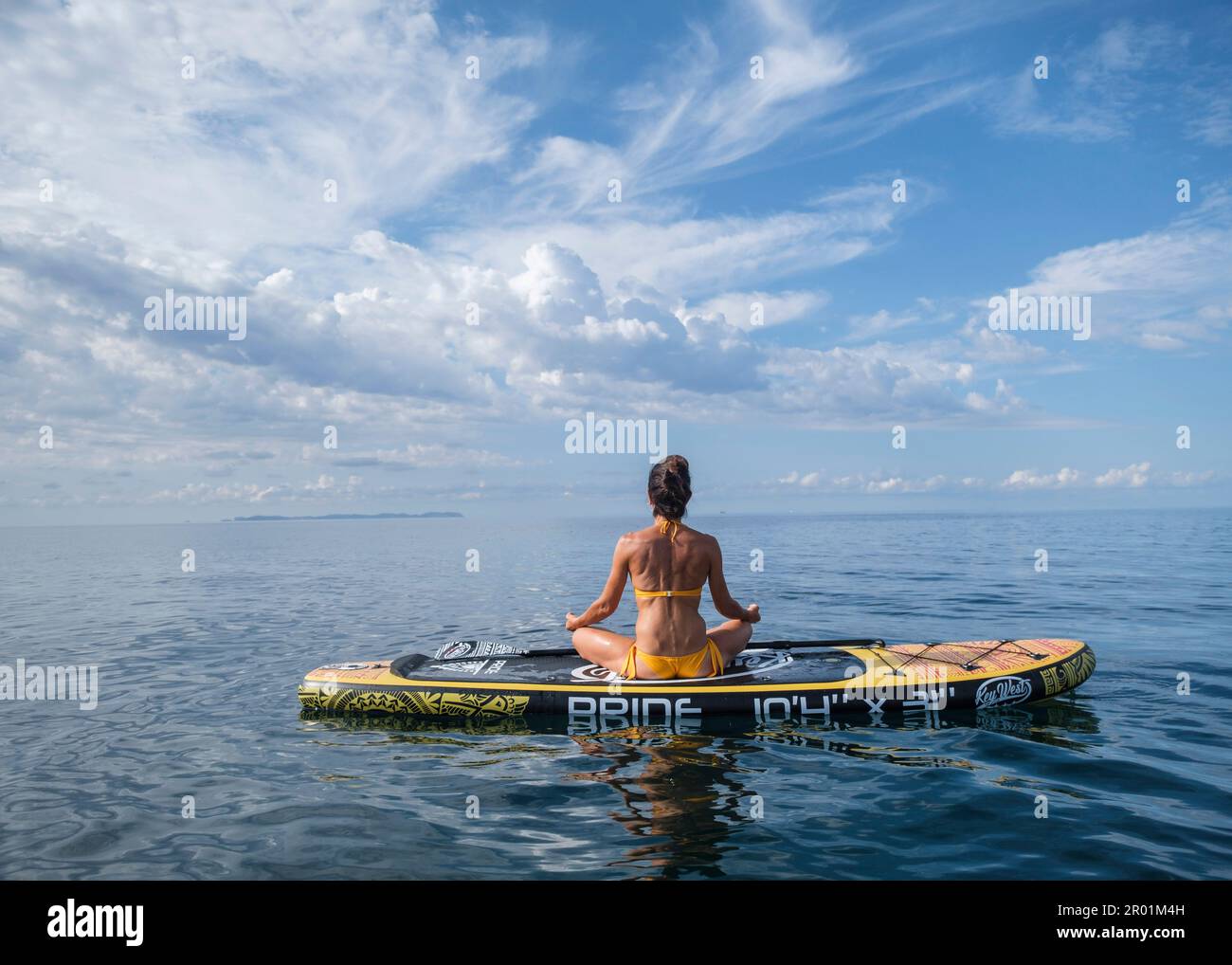 Donna che pratica yoga su una tavola da surf sotto un cielo drammatico, Estalella, costa di Llucmajor, Maiorca, Isole Baleari, Spagna. Foto Stock