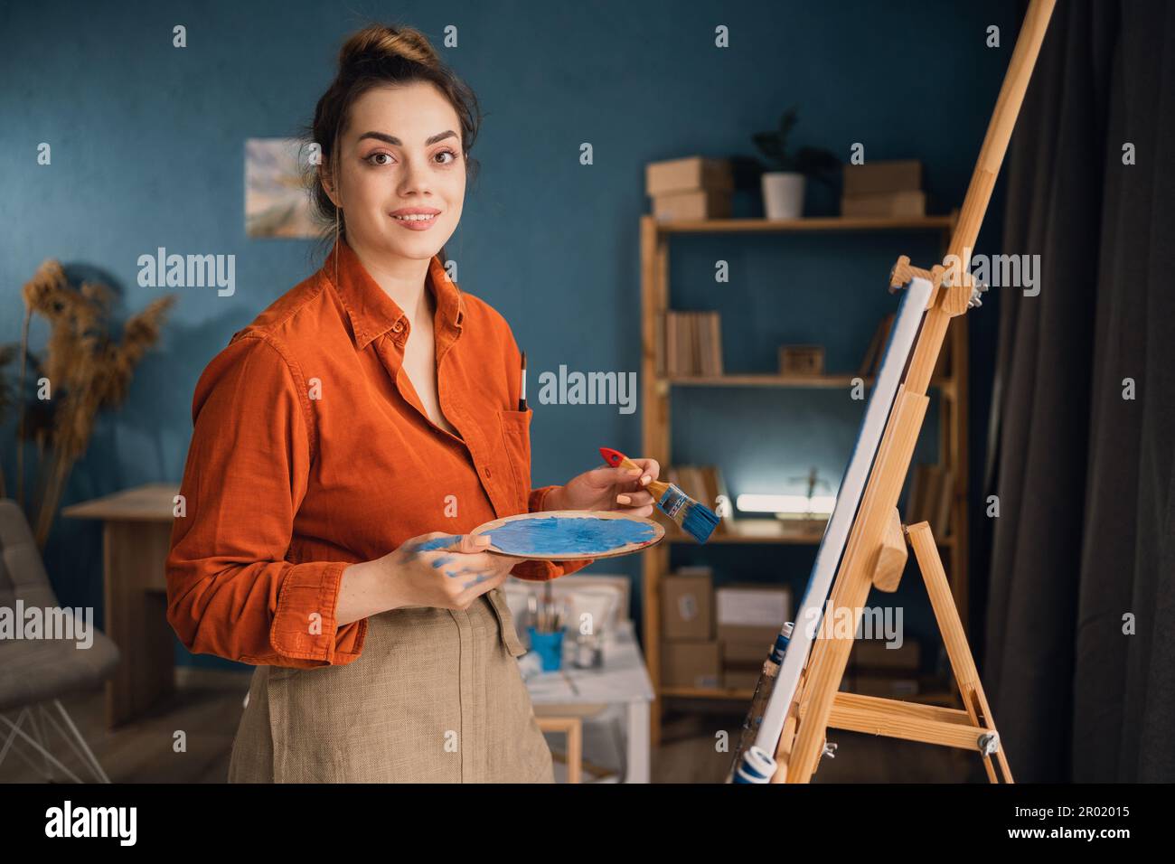 una giovane studentessa è impegnata in uno studio d'arte a casa, imparando a dipingere paesaggi, cercando di mescolare diversi acquerelli su cartone. A. Foto Stock
