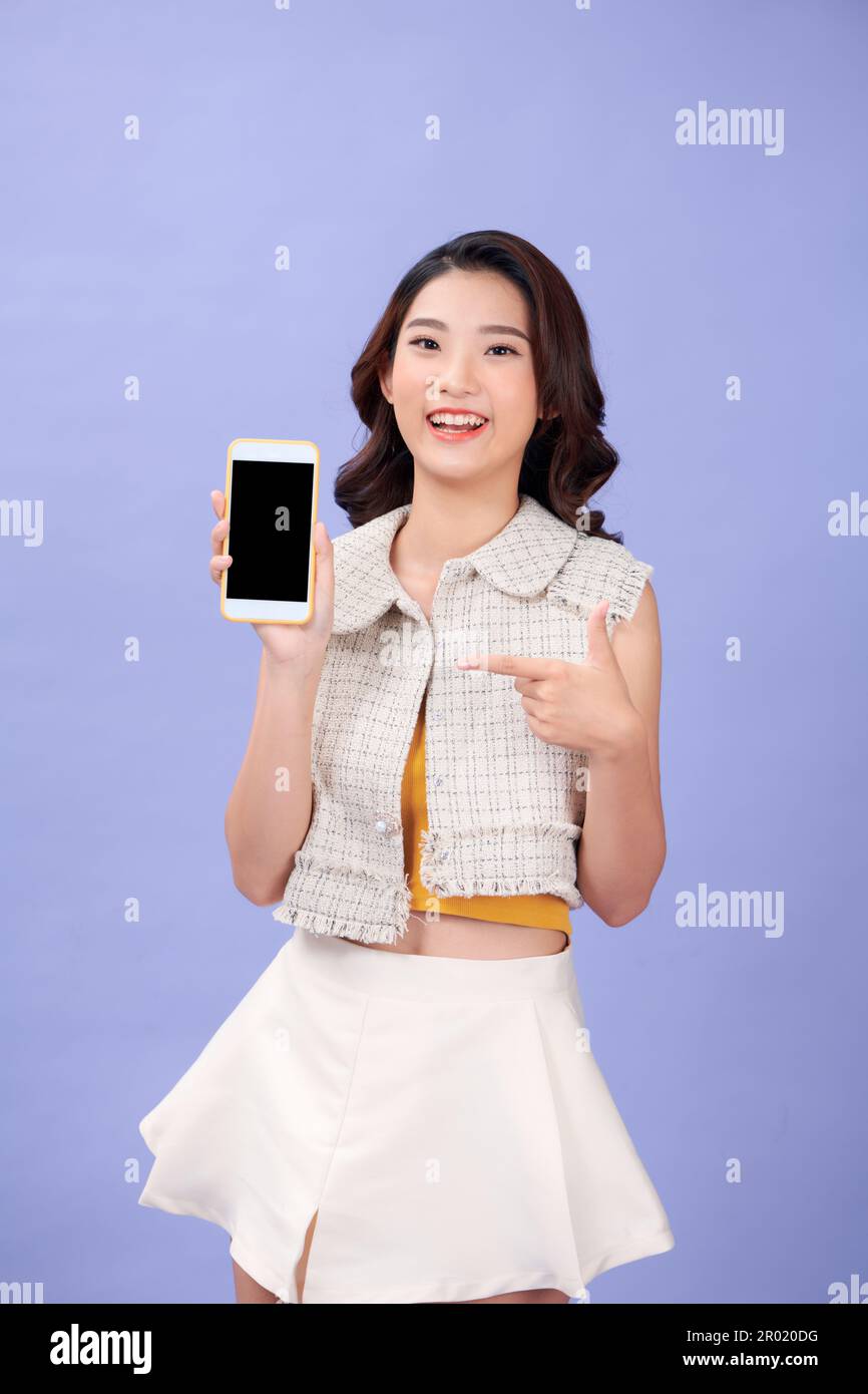 Giovane donna sorridente attraente sta puntando sullo schermo vuoto del telefono nella sua mano Foto Stock