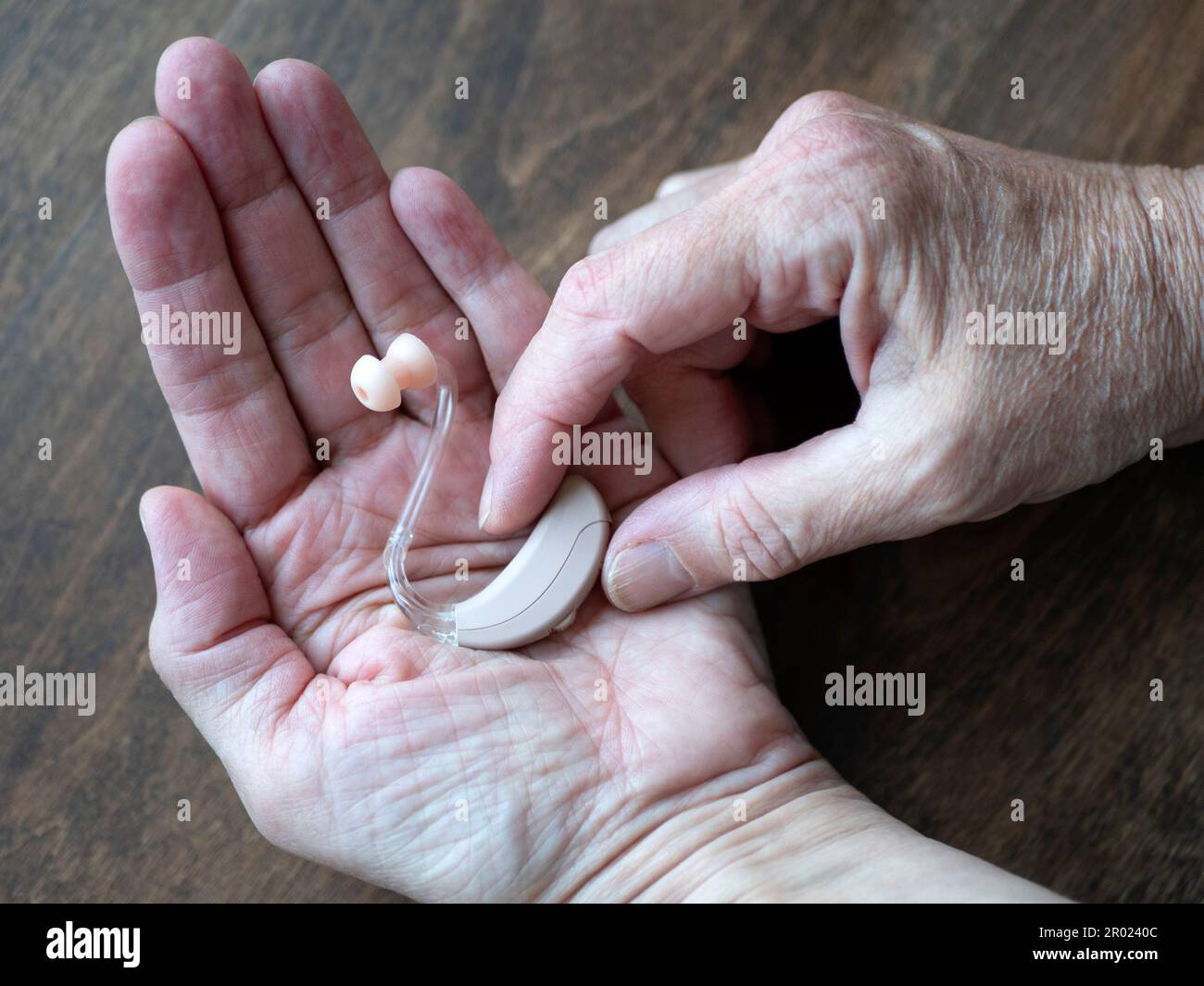 Uso di un apparecchio acustico a causa di una compromissione dell'udito peggiorata. Le mani impugnano l'apparecchio acustico, primo piano Foto Stock