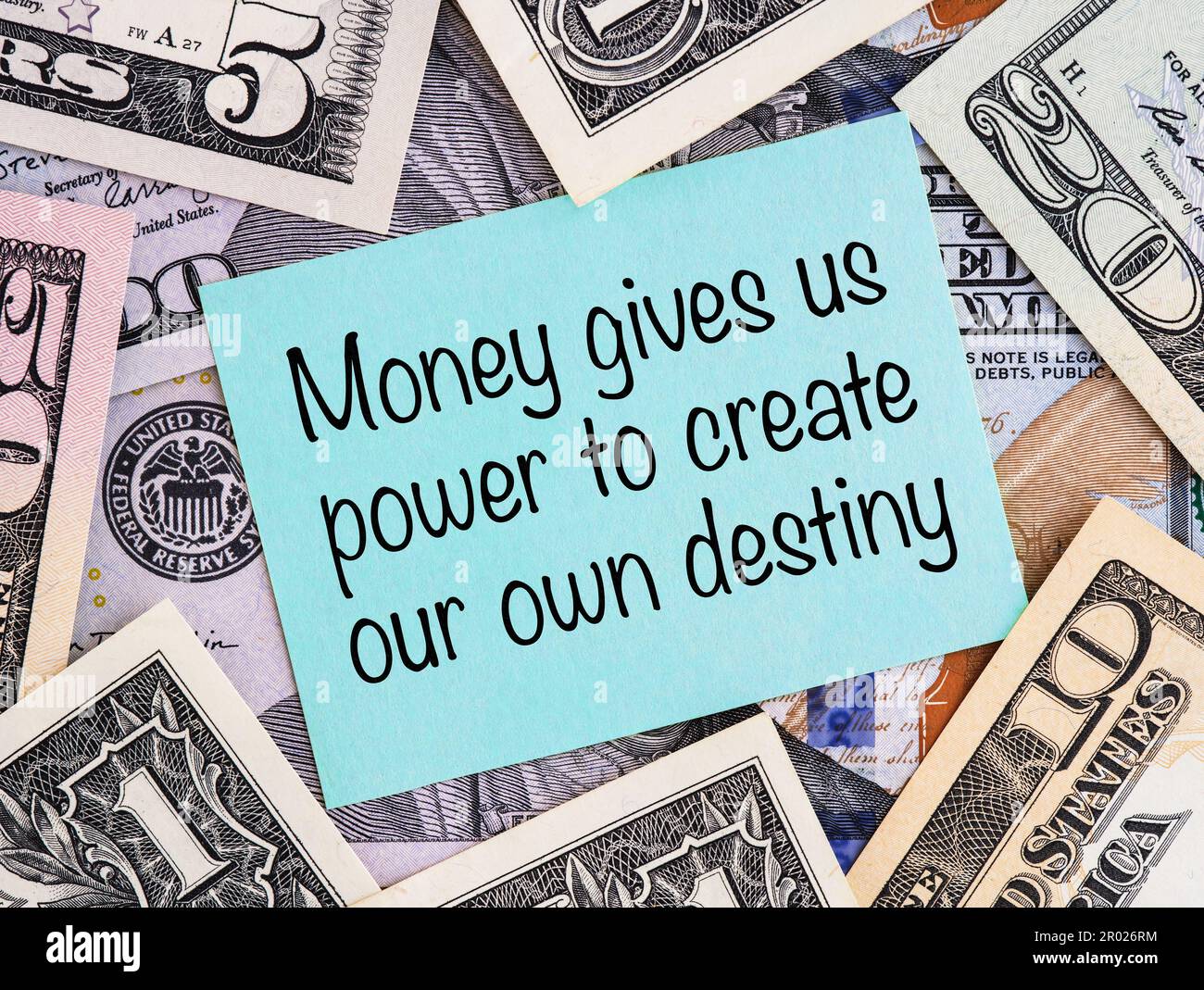 Una nota di carta blu con la frase soldi ci dà il potere di generare il nostro proprio destino su uno sfondo delle fatture del dollaro degli Stati Uniti. Foto Stock
