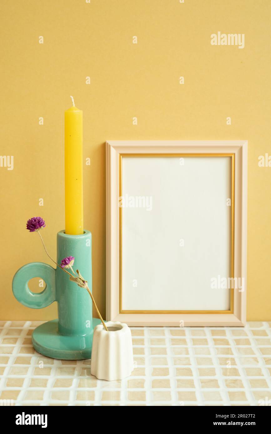 Cornice vuota e candela, fiore sul tavolo di tessere di controllo. sfondo giallo parete Foto Stock