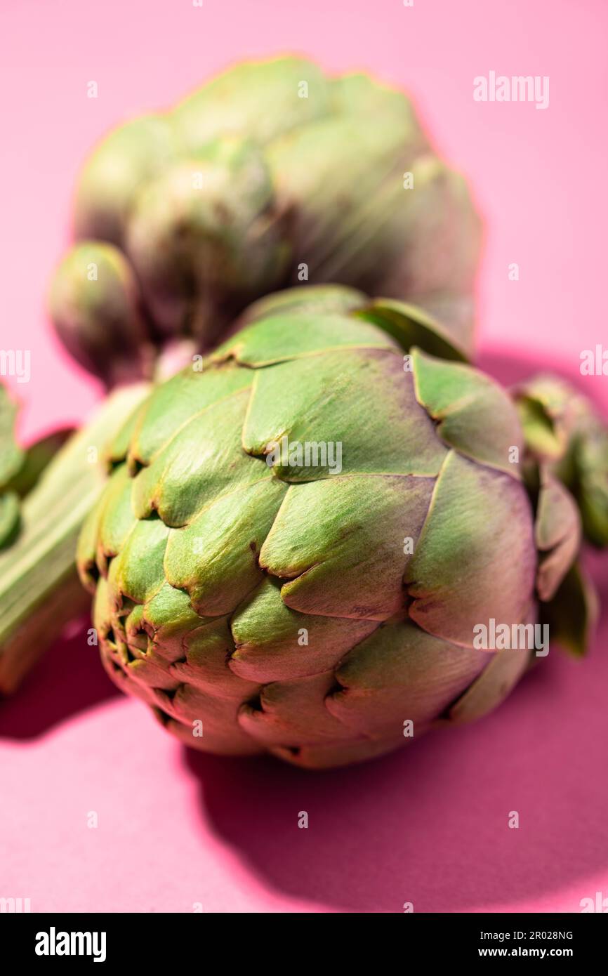 Carciofi freschi verdi isolati su sfondo rosa Foto Stock