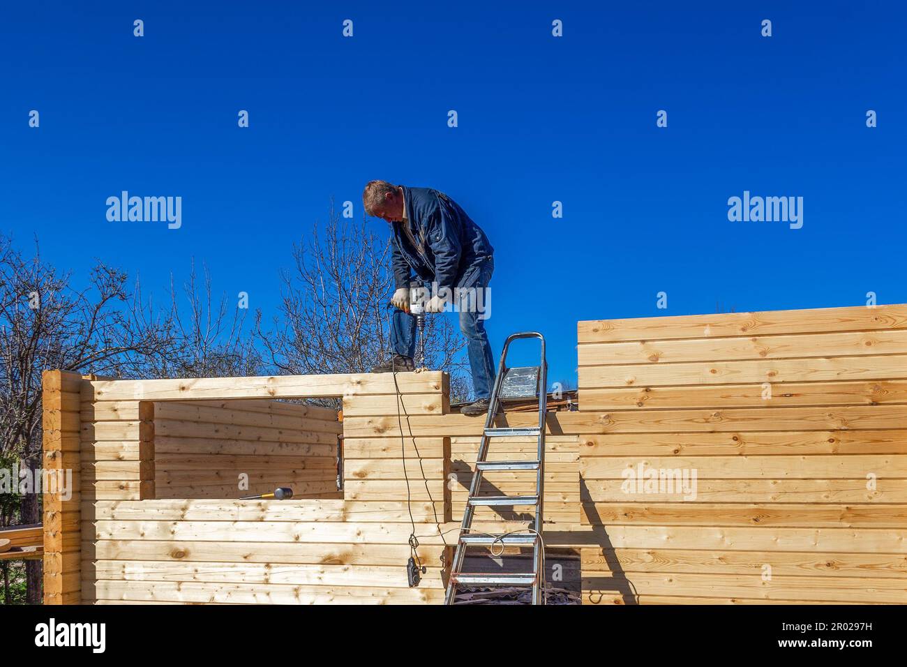 un uomo costruisce una casa in legno profilato in campagna contro il cielo blu Foto Stock