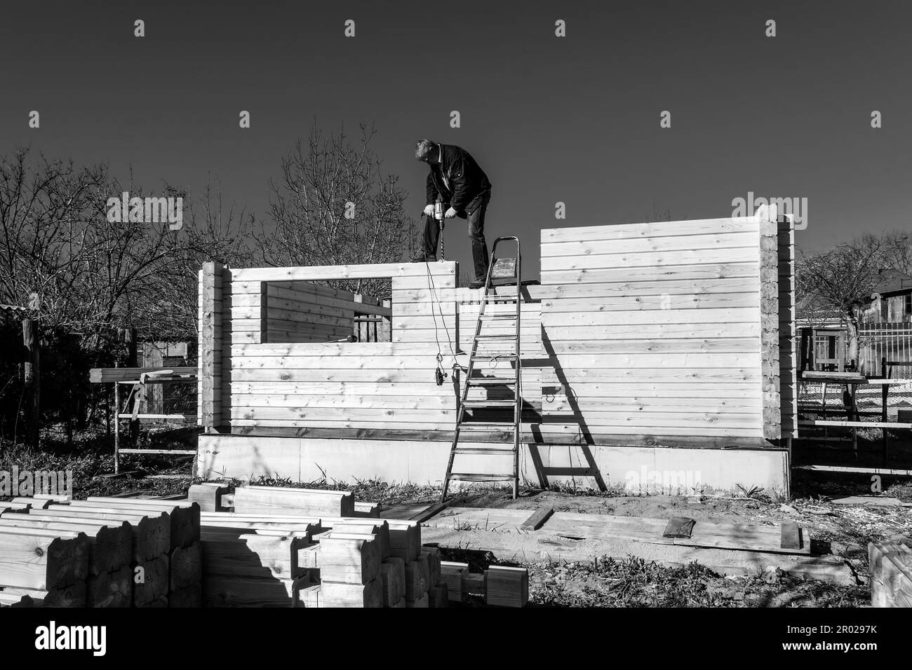 un uomo costruisce una casa in legno profilato in campagna contro il cielo blu, foto in bianco e nero Foto Stock