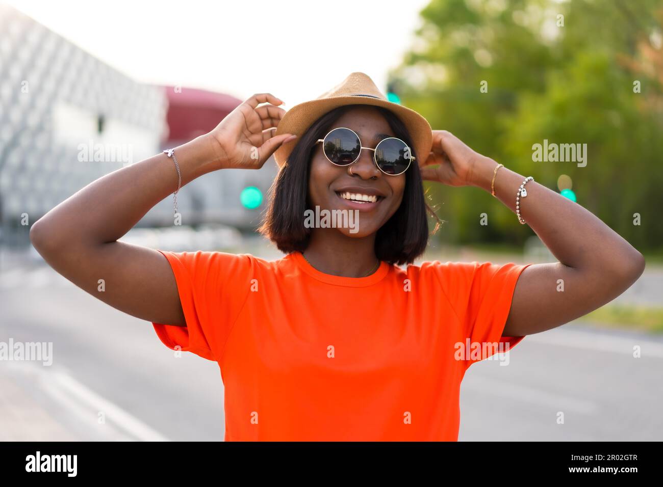 Vibrazioni estive: Giovane donna nera turista in t-shirt verde e occhiali da sole contro parete marrone, foto lifestyle Foto Stock