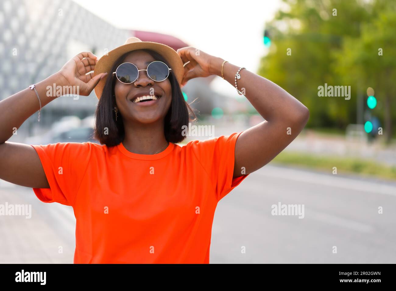 Giovane donna nera turista con t-shirt arancione e occhiali da sole godendo l'estate in città, foto lifestyle Foto Stock