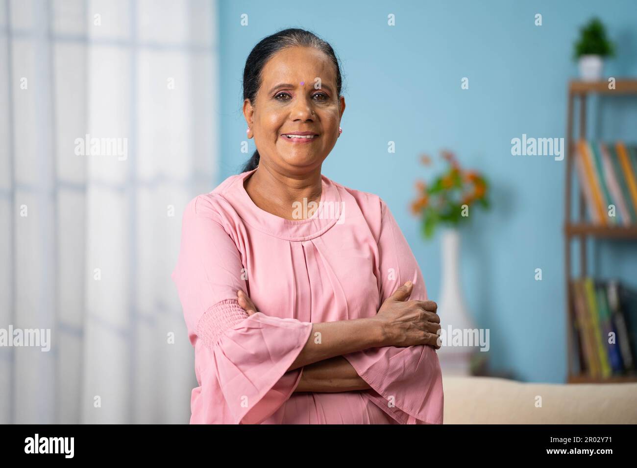 Ritratto scatto di felice sorridente donna anziana indiana fiduciosa in piedi con le braccia incrociate guardando la macchina fotografica a casa - concetto di soddisfazione Foto Stock