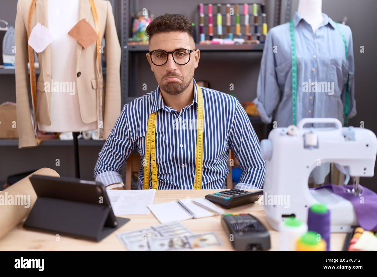 Uomo ispanico con Beard dresssaker designer che lavora presso atelier depresso e la preoccupazione per il disagio, piangendo arrabbiato e paura. espressione triste. Foto Stock