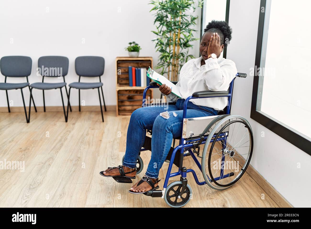 Giovane donna nera seduta su sedia a rotelle in sala d'attesa sbadigliando  stanco coprendo mezza faccia, occhio e bocca con la mano. faccia fa male  nel dolore Foto stock - Alamy