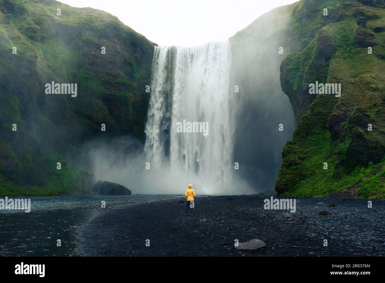Scenografico scenario della cascata di Skogafoss che scorre con una donna asiatica in piedi in estate in Islanda Foto Stock
