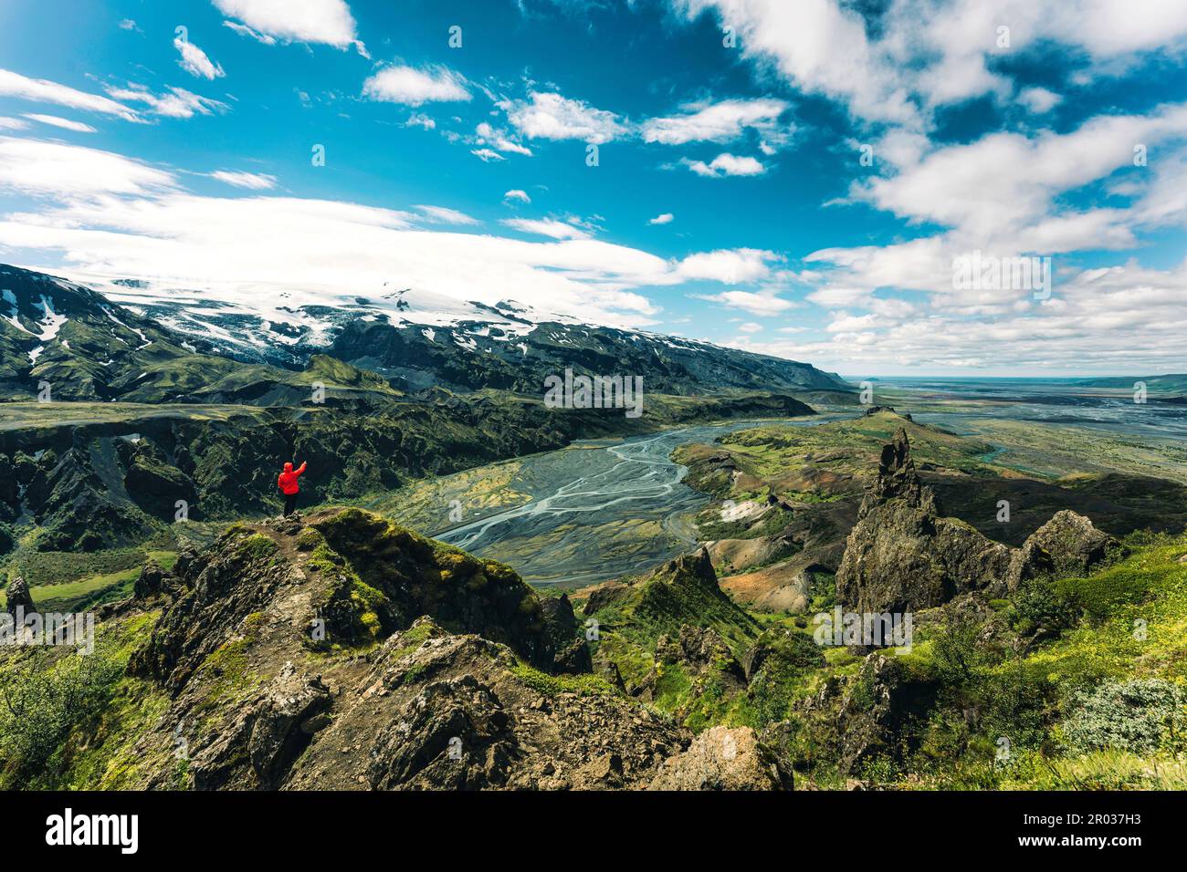 Spettacolare vista dell'uomo Hiker in giacca rossa che si erge sulla cima del punto panoramico di Valahnukur circondato dalla montagna vulcanica e dal fiume Krossa in Highlan islandese Foto Stock