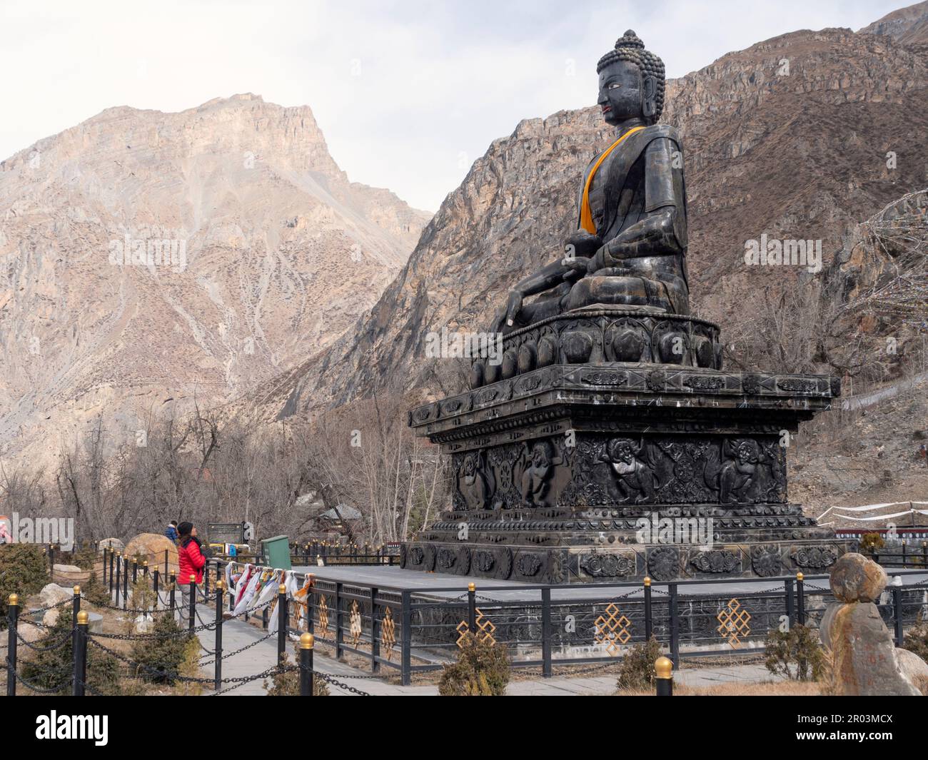 Vista orizzontale di una donna zaino in spalla a Muktinath, Nepal, in preghiera a Namaste mudra di enorme Buddha di pietra. Foto Stock