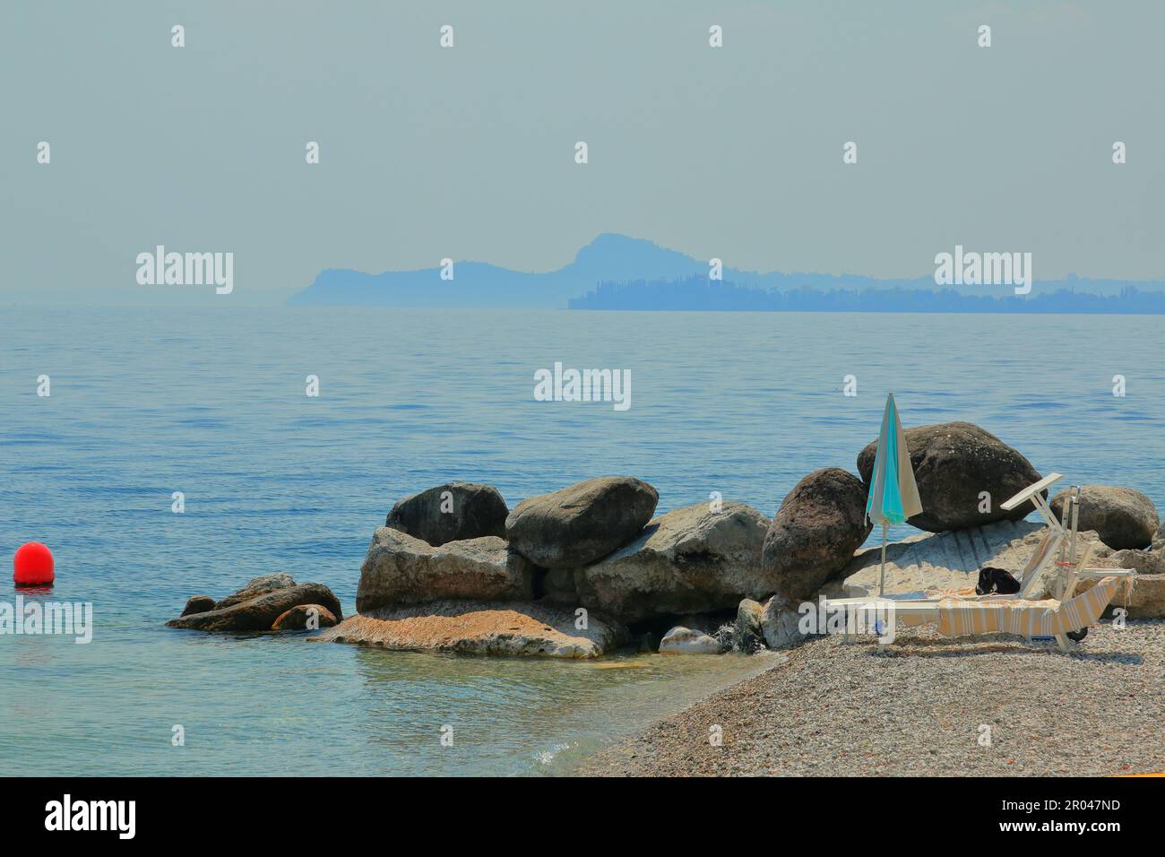 Lettini da mare e ombrellone a Maderno sul Lago di Garda. Dietro di loro sono grandi pietre. Foto Stock