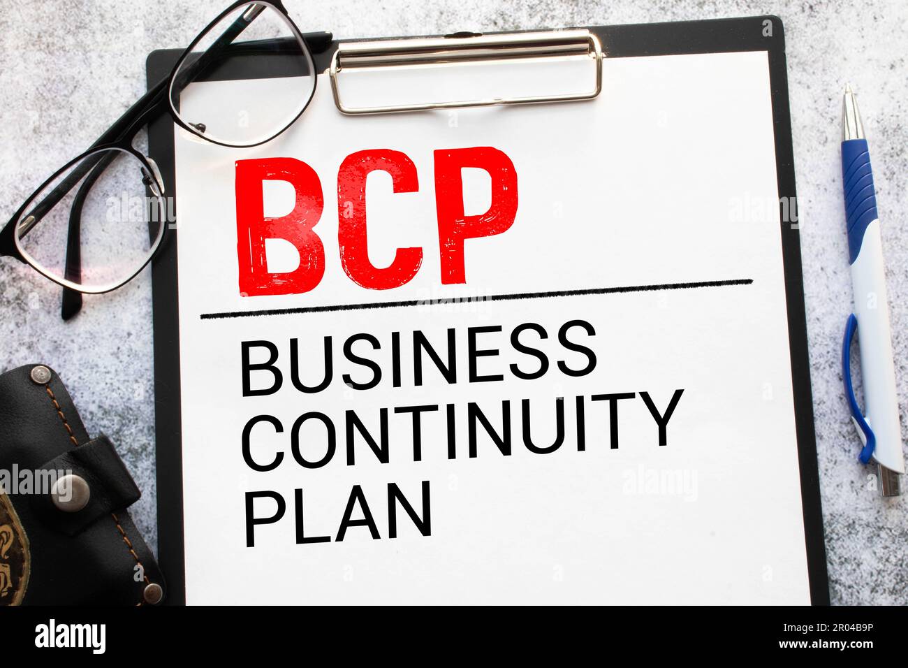 Su un tavolo da ufficio di colore chiaro si trova un computer, una calcolatrice nera, una penna e un notebook con il testo BCP Business Continuity Plan Foto Stock