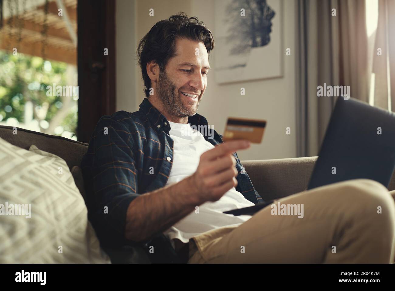 Signor grande spender. un bel giovane uomo che usa il computer portatile e la carta di credito mentre si rilassa su un divano a casa. Foto Stock
