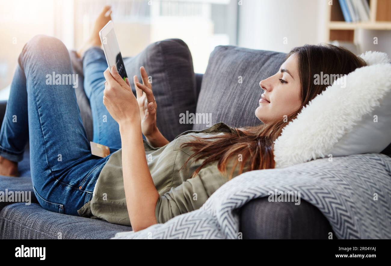 La ricerca per quello cattura il suo occhio. una bella giovane donna che usa il suo tablet digitale mentre si rilassa a casa. Foto Stock