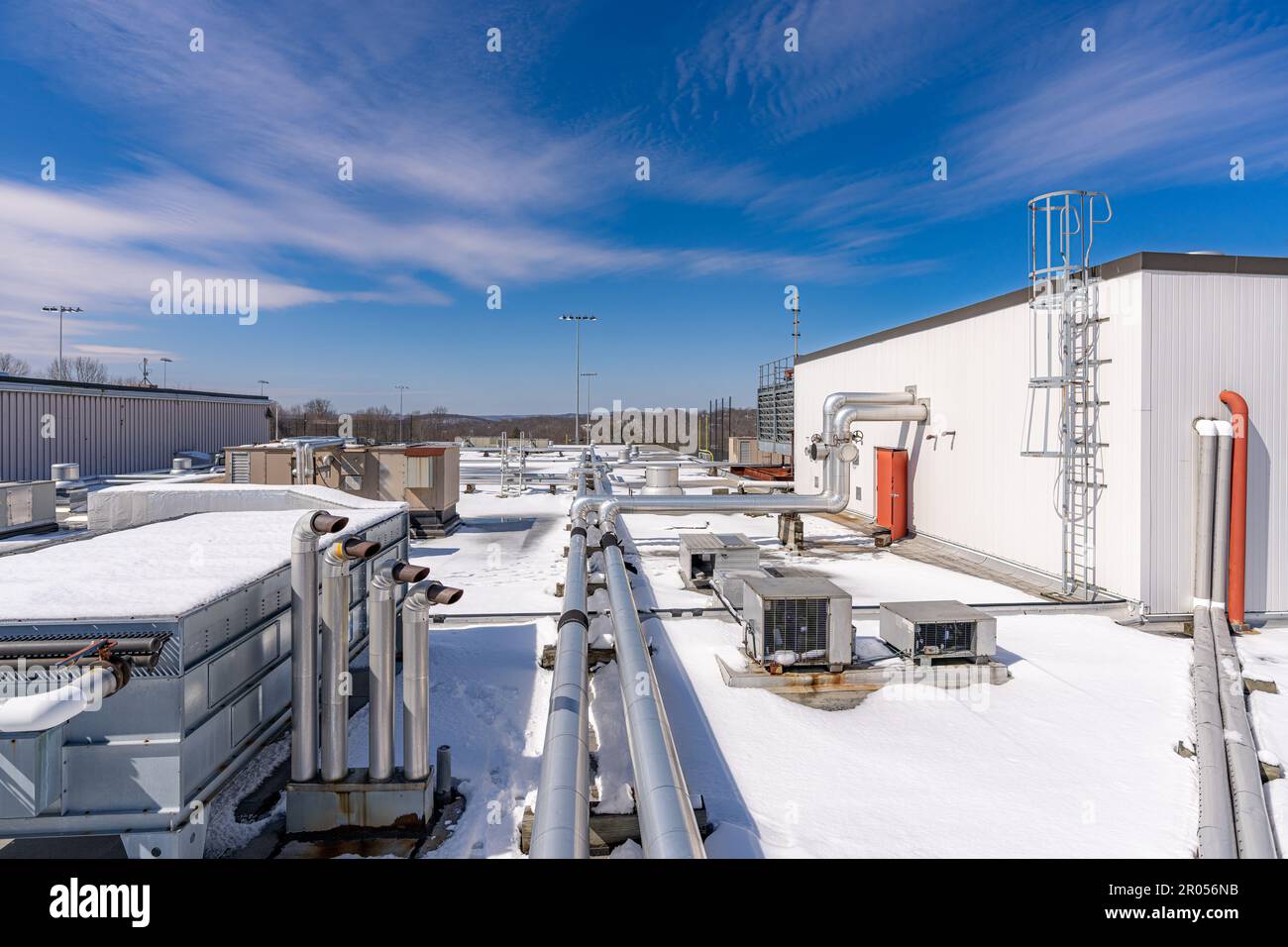 Foto di un impianto di ventilazione e tubazioni di scarico sul tetto in un edificio commerciale coperto di neve Foto Stock