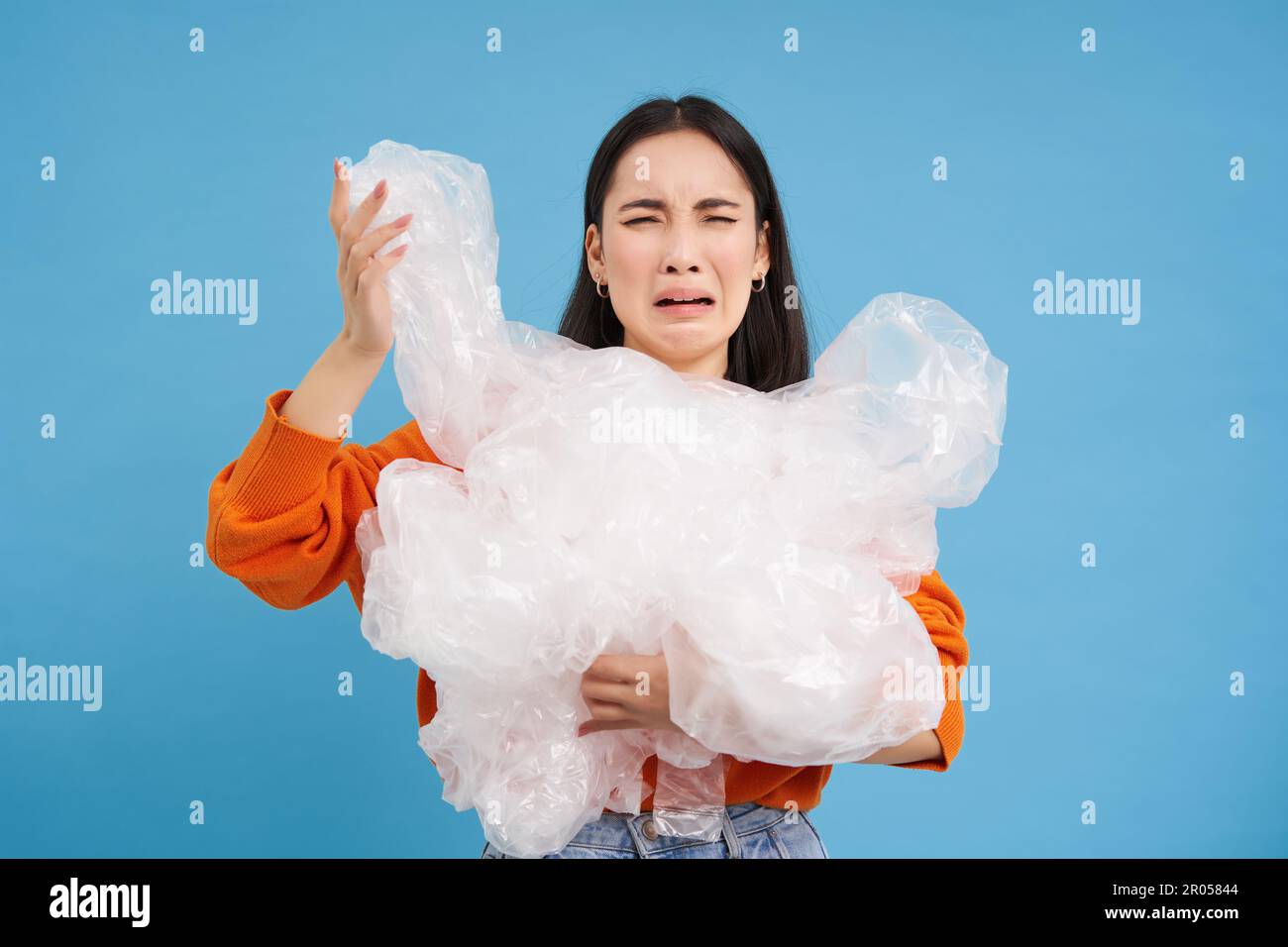 Donna asiatica piangente con rifiuti di riciclaggio di plastica, stanco di smistamento rifiuti in diversi contenitori, preservando la natura, sfondo blu. Foto Stock