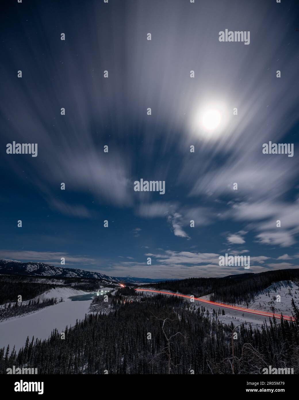 Scena notturna di una strada invernale nel Canada settentrionale, territorio dello Yukon. Preso sulla notte illuminata dalla luna con cielo stellato blu luminoso, abete rosso, alberi che circondano. Foto Stock