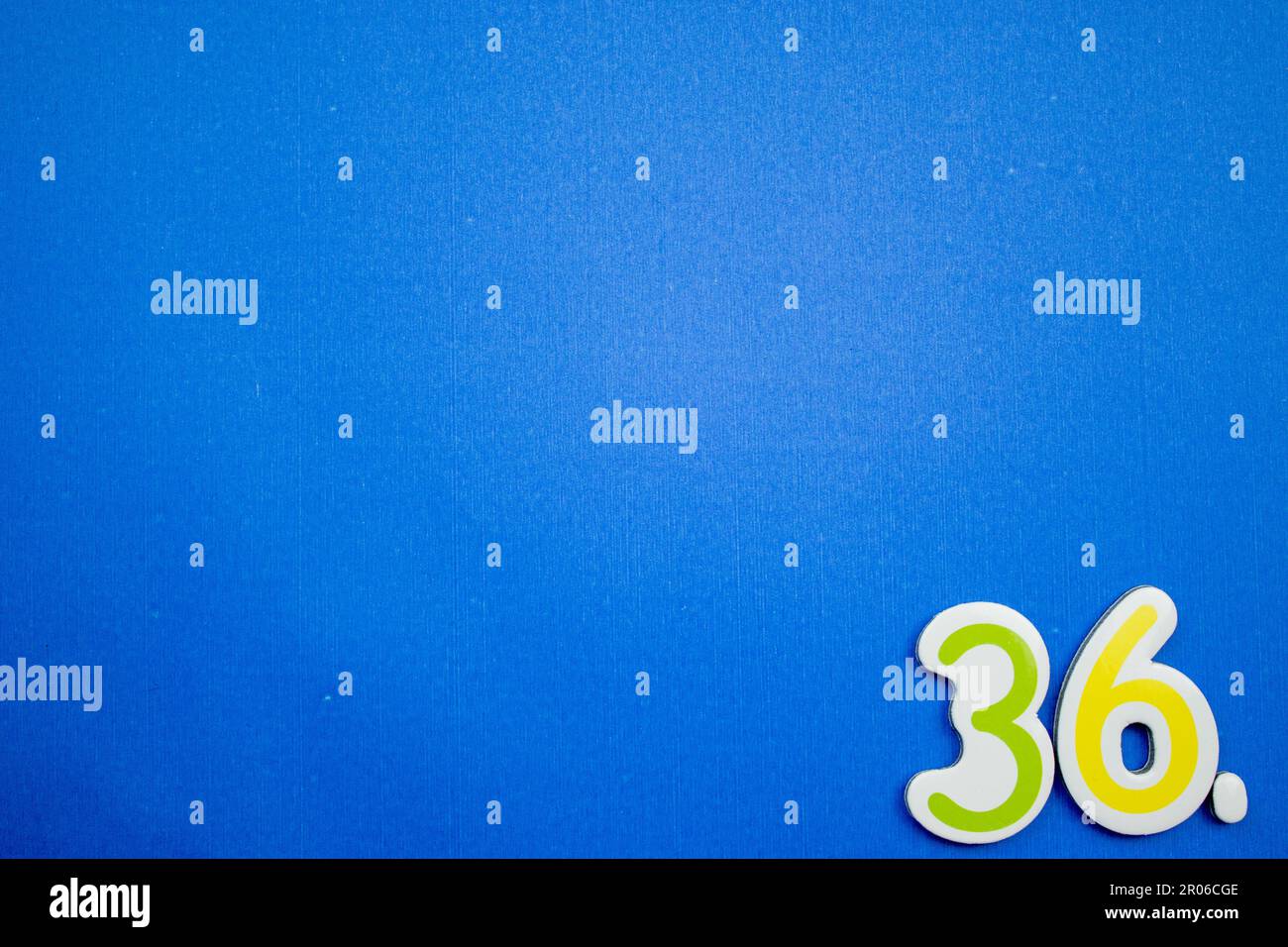 Il numero 36, verde e giallo, fotografato dall'alto, posto sul bordo di uno sfondo blu. Foto Stock