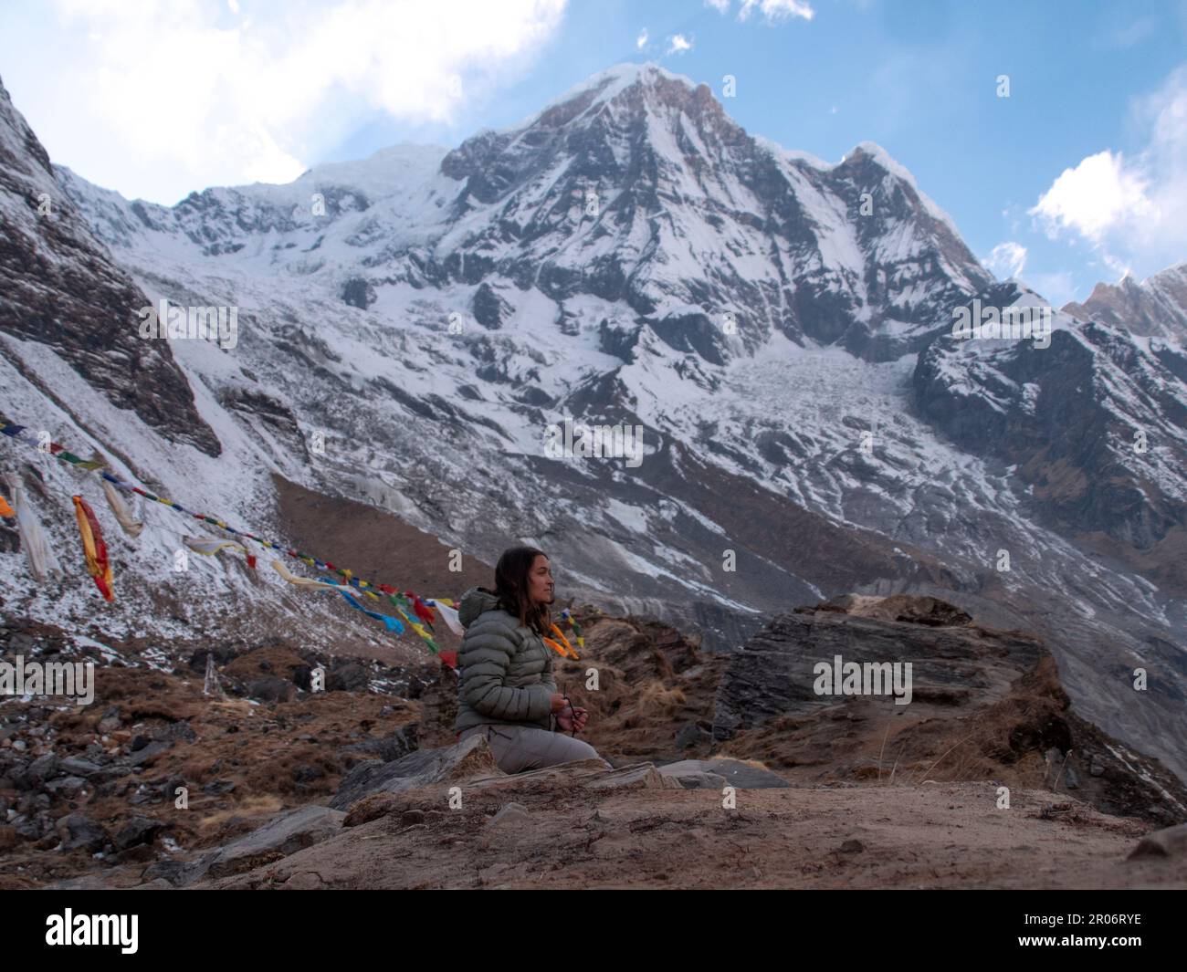 Donna zaino in spalla seduto nel campo di base Annapurna facendo una meditazione per ringraziare gli spiriti della natura dopo tutto lo sforzo che ha preso per arrivare lì. Foto Stock