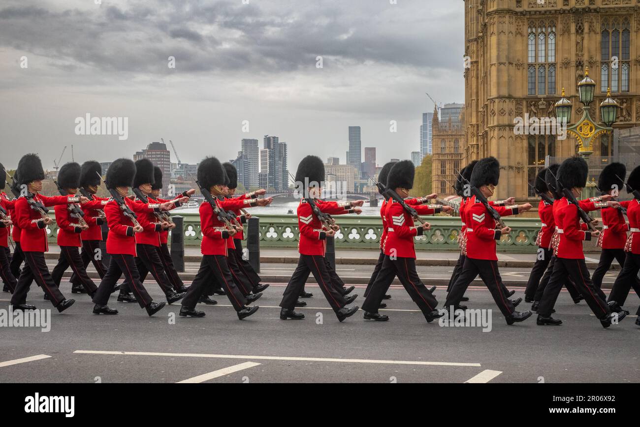 Con i loro fucili, i soldati delle Guardie Grenadier dell'Esercito britannico marciano in costume cerimoniale attraverso il Westminster Bridge e oltre le Case Foto Stock