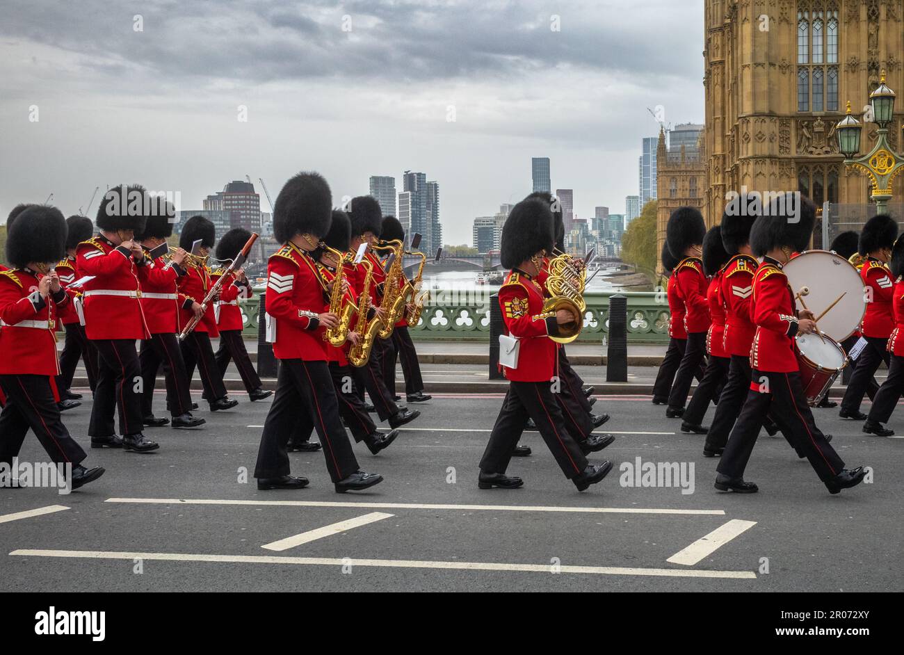Mentre marciano in uniforme cerimoniale attraverso il Westminster Bridge, una band appartenente alla Grenadier Guards dell'Esercito britannico suona musica, mentre marciano Foto Stock
