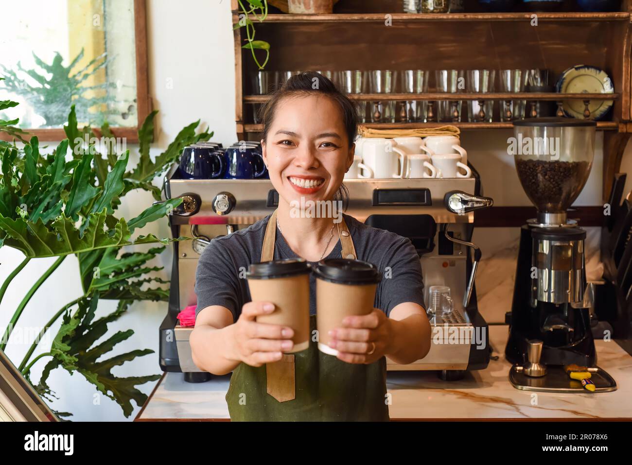 Cameriera vietnamita sorridente che tiene tazze di carta con caffè in un bar Foto Stock