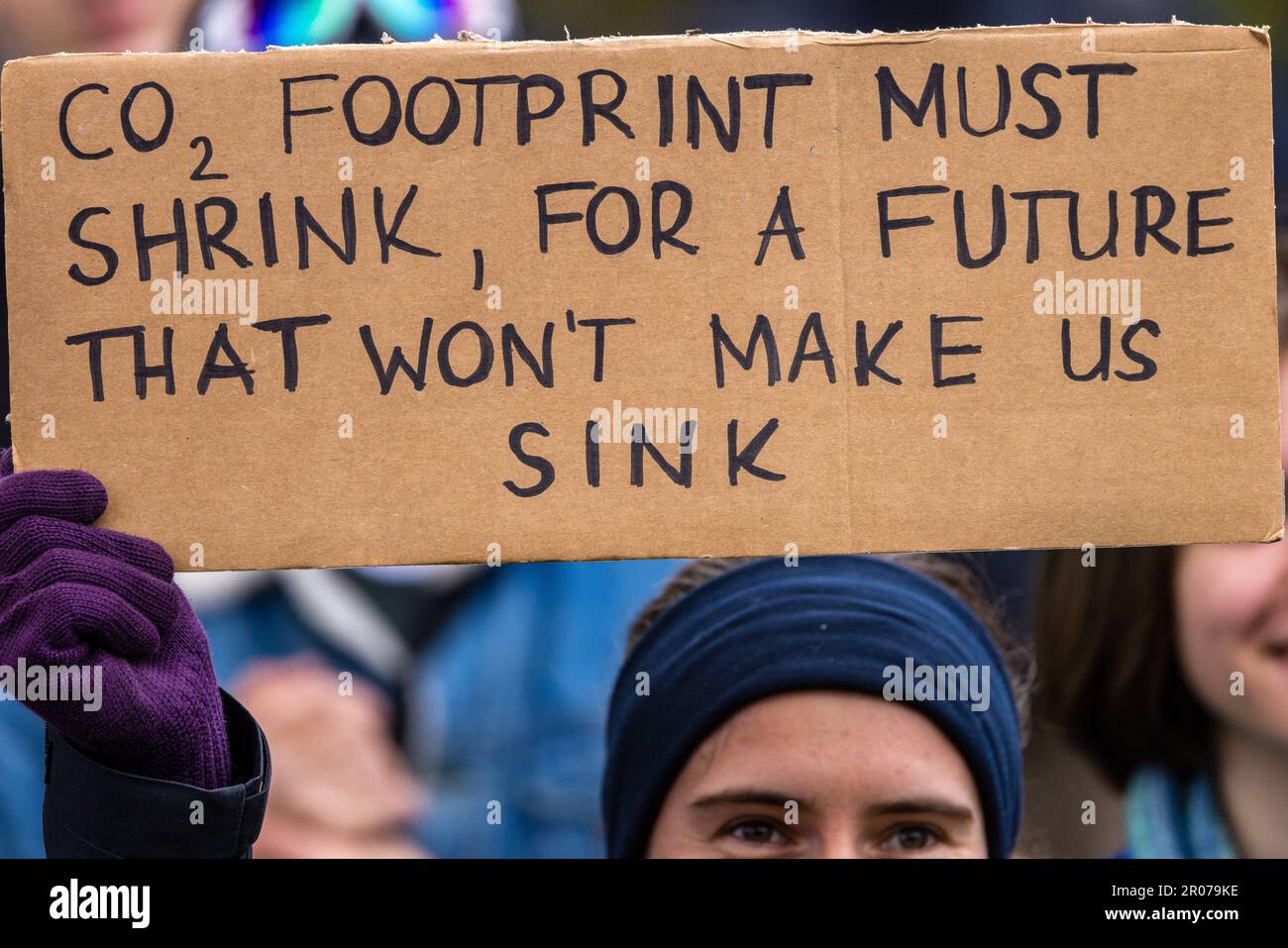 07 maggio 2023, Sassonia, Schleife: 'CO2 l'impronta deve ridursi per un futuro che non ci farà sprofondare' è scritto su un cartello portato da un partecipante ad una dimostrazione. Un'alleanza di associazioni ambientaliste, gruppi climatici e iniziative locali aveva richiesto una dimostrazione presso la miniera a cielo aperto di Nochten a Lusatia. Tra gli altri, venerdì per il futuro, Greenpeace, Campact, BUND Sassonia, VI partecipano Grüne LIGA, alle Dörfer bleiben, serbski sejm. L'alleanza chiede una graduale eliminazione del carbone nella Germania orientale rispetto al 2038, affermando che il cambiamento strutturale deve offrire ai cittadini della regione sus Foto Stock