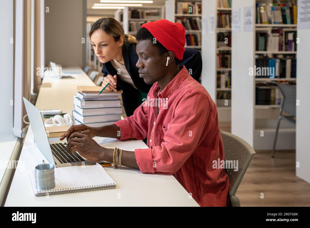 Interessato afro-americano che scrive sul laptop vicino a messo a fuoco insegnante dell'università che guarda lo schermo Foto Stock