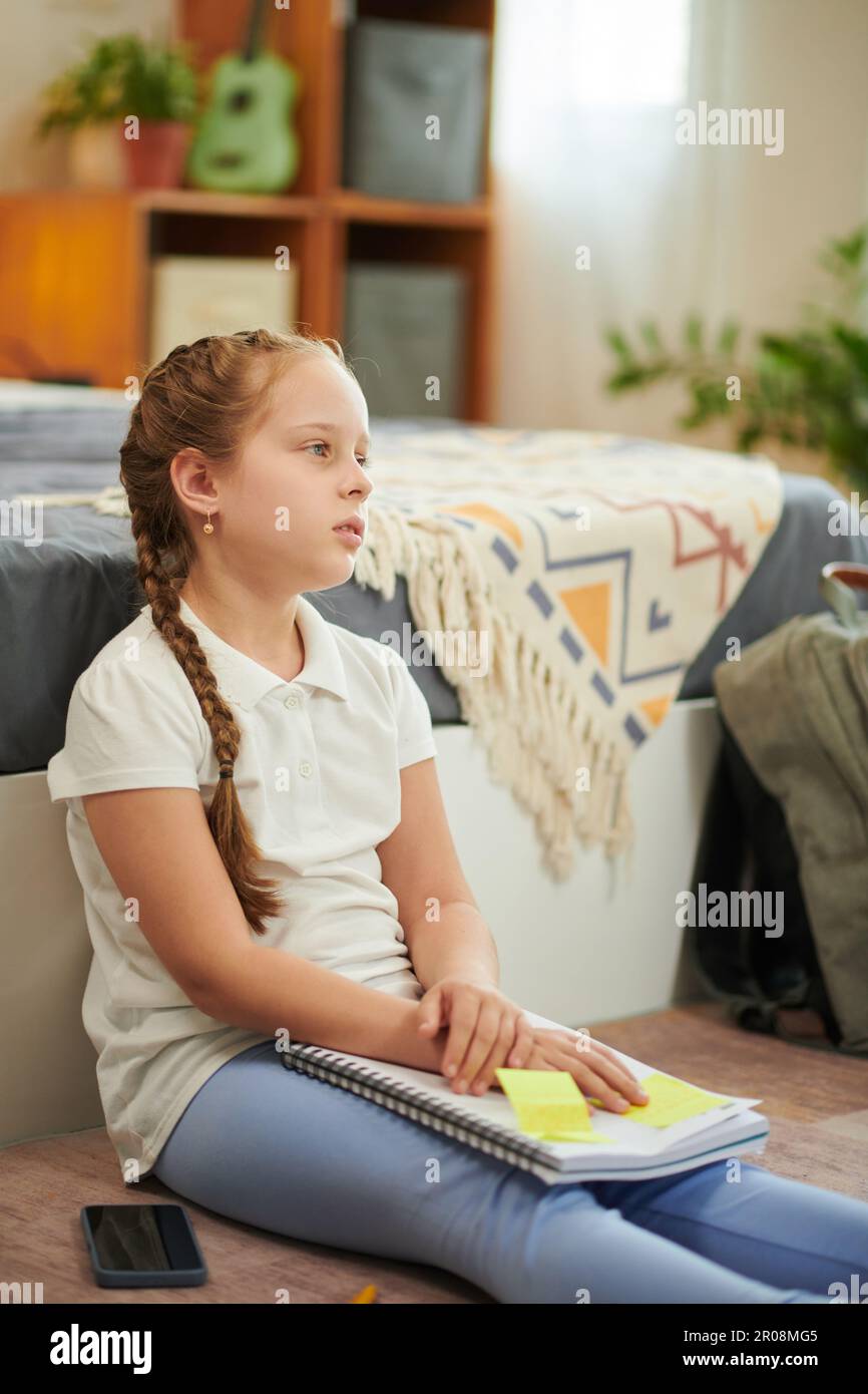Ragazza stanca dopo aver fatto i compiti seduti sul pavimento nella sua camera da letto Foto Stock