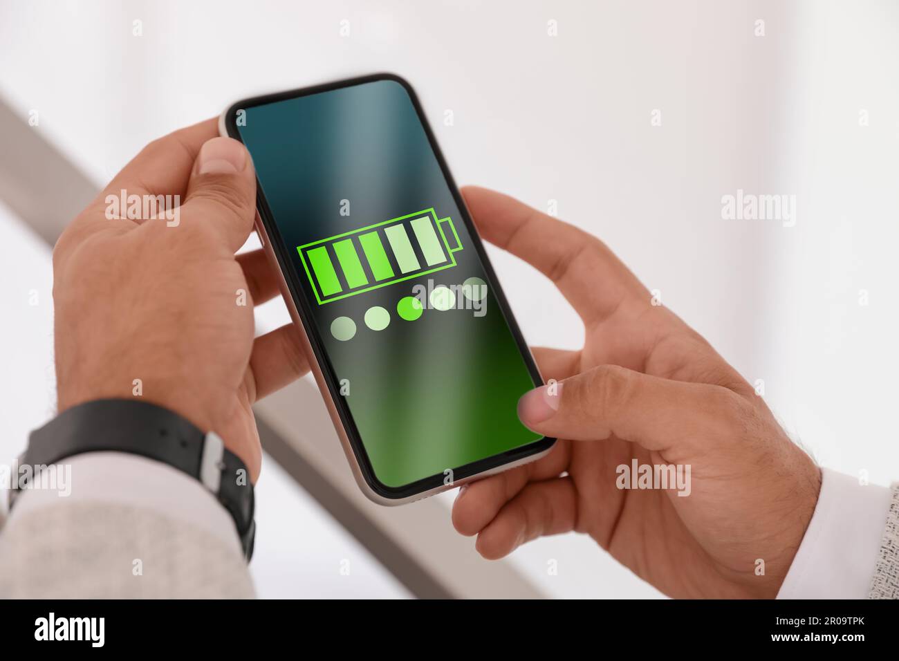 Giovane uomo che tiene uno smartphone con batteria completamente carica in ambienti chiusi, primo piano Foto Stock