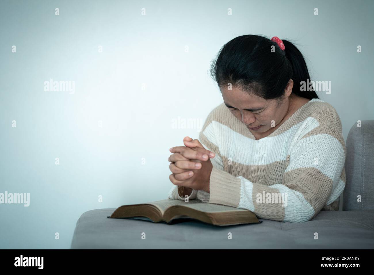 donna che si inginocchia e prega in casa moderna al tramonto. La preghiera femminile cattolica adorazione a Dio augura una vita migliore in casa all'alba con fede credente Foto Stock