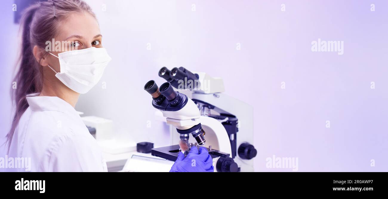Una giovane donna medica (assistente di laboratorio) conduce uno studio di un campione di sangue su un microscopio. Molto spazio vuoto Foto Stock