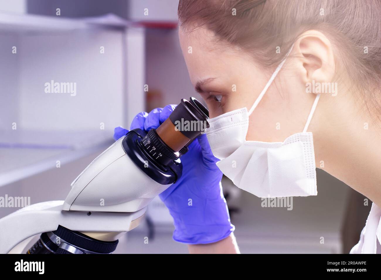 Una giovane donna medica (assistente di laboratorio) conduce uno studio di un campione di sangue su un microscopio. Primo piano guardando un microscopio Foto Stock