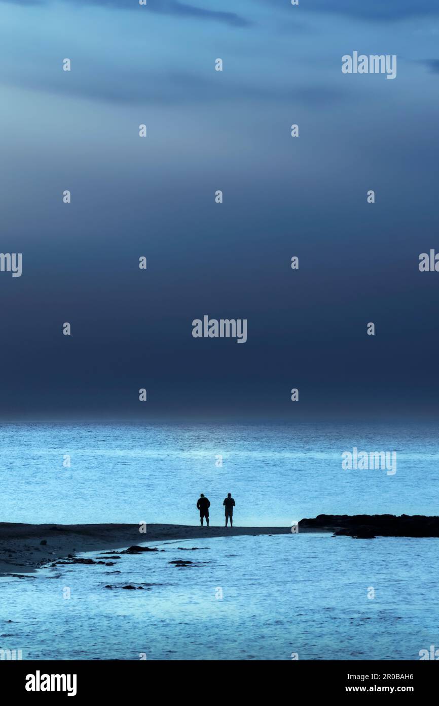 Due uomini che si affacciano sul mare dalla spiaggia verso una tempesta imminente. Foto Stock