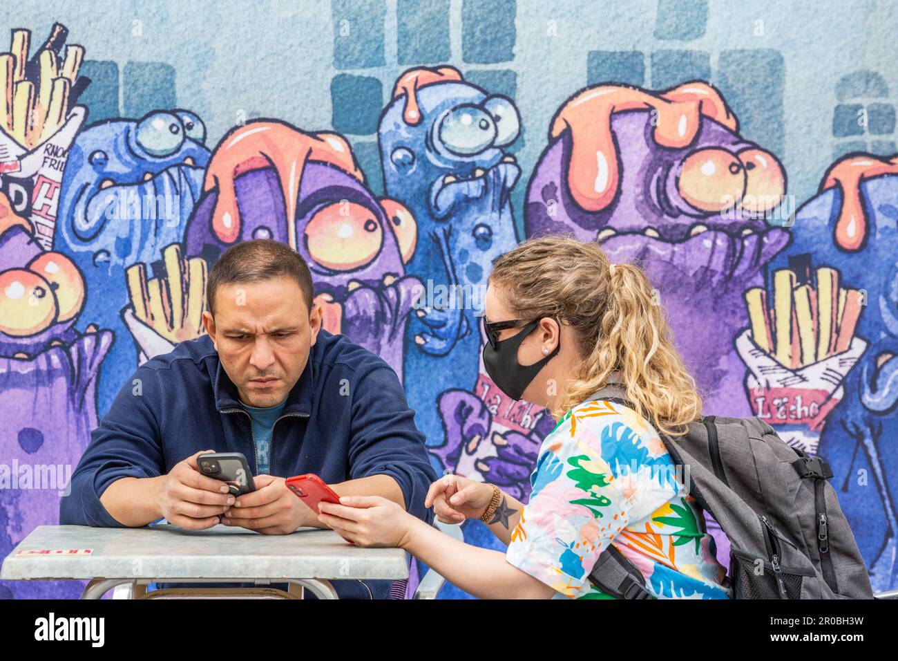 Coppia seduto a confrontare le informazioni dai loro telefoni cellulari di fronte a un affresco con Kid paddle motivi. Bruxelles. Foto Stock