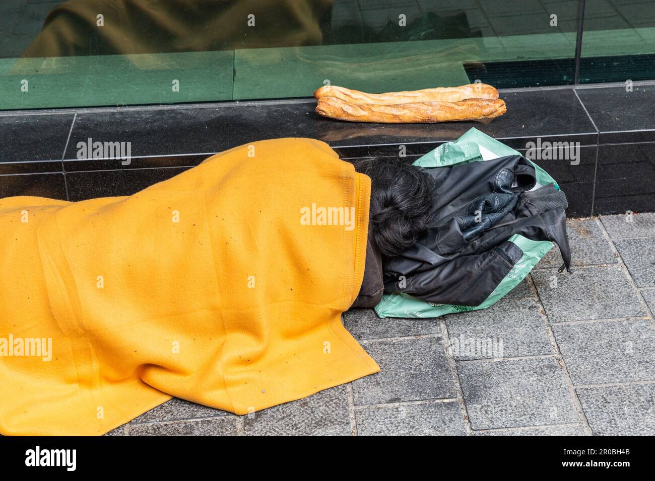 Uomo senza casa che dorme per strada sotto una coperta arancione, le sue due baguette accanto a lui. Bruxelles. Foto Stock