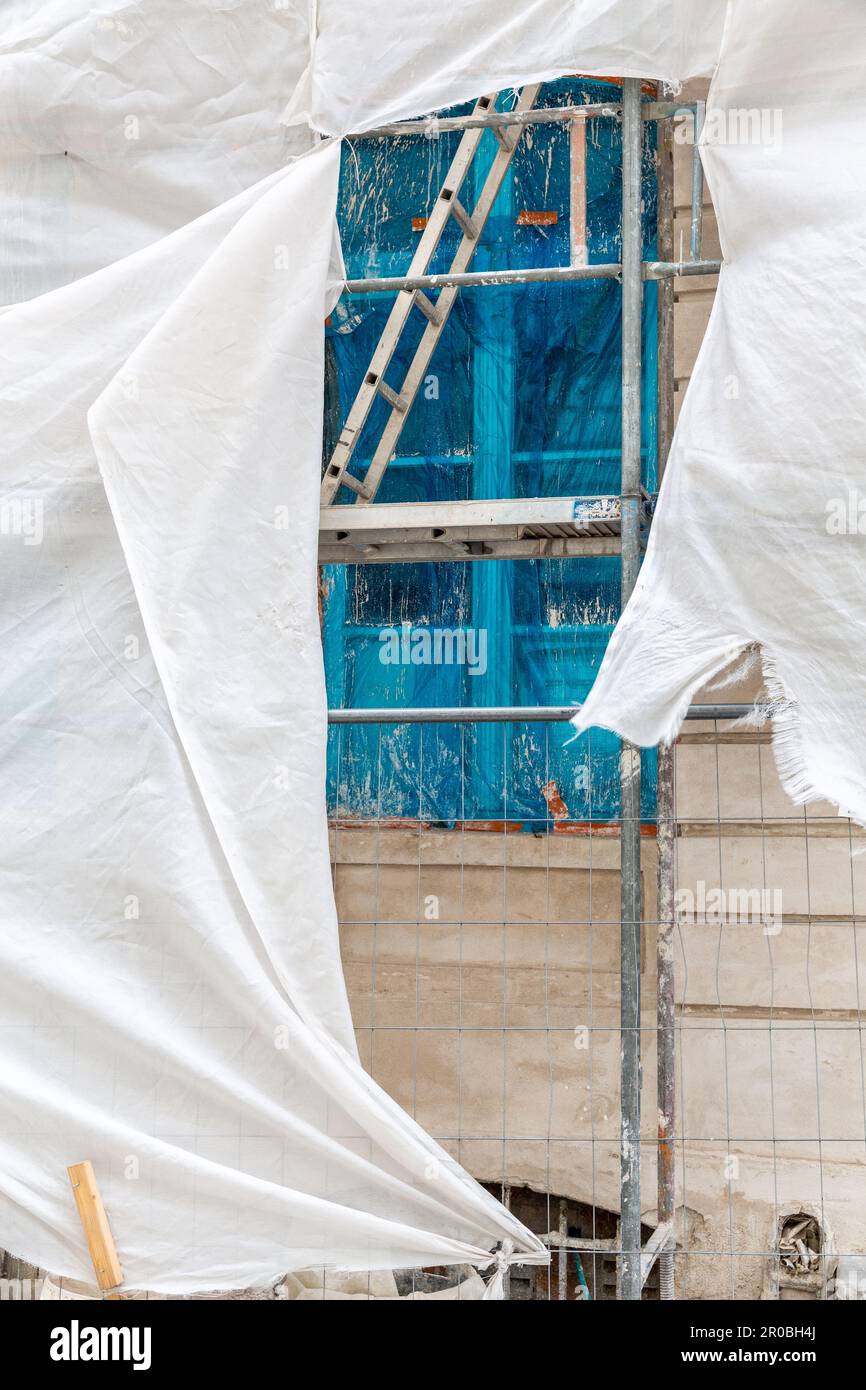 Finestra protetta da una pellicola blu, dietro l'impalcatura di un edificio in riparazione. Bruxelles. Foto Stock