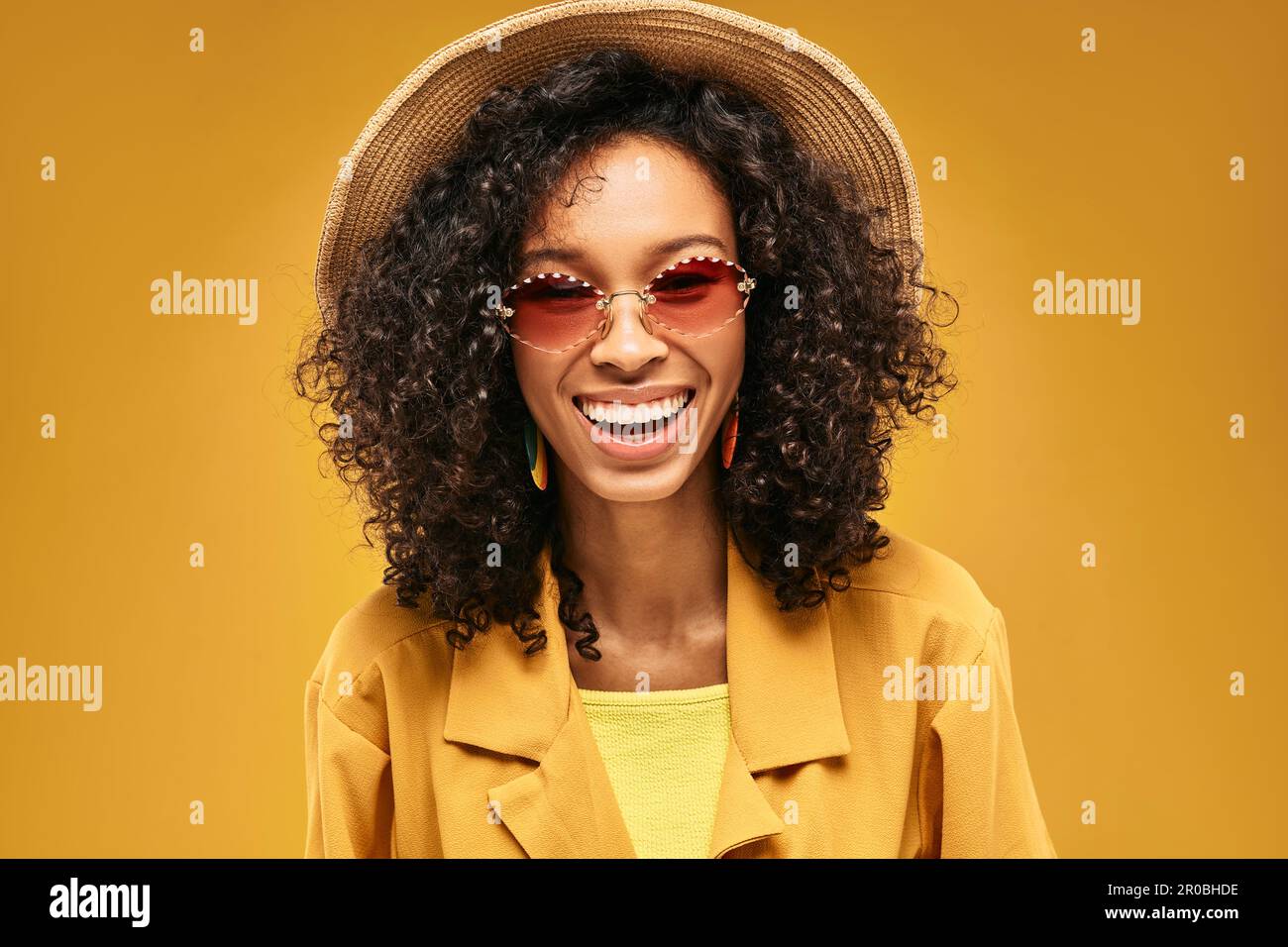 Concetto di viaggio. Ritratto di ridente ragazza afro-americana in cappello di paglia e occhiali da sole rosa andando presto al resort turistico Foto Stock