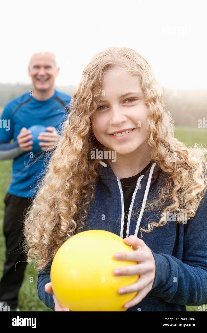 Ragazza adolescente con il padre che si esercita con la palla di yoga sul campo e sorridente durante l'alba, Baviera, Germania Foto Stock
