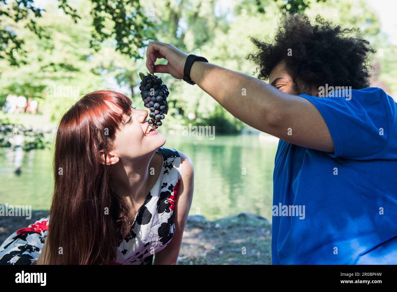 Uomo che nutra l'uva alla donna al lago nel Giardino Inglese di Monaco, Germania Foto Stock