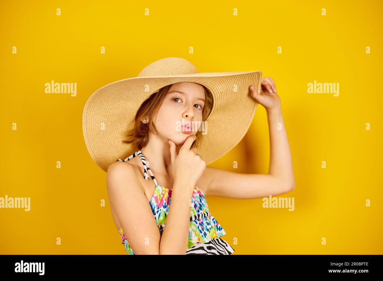 Ragazza adolescente bambino in costume da bagno e cappello di paglia in posa in studio su sfondo giallo, umore estivo, Foto Stock