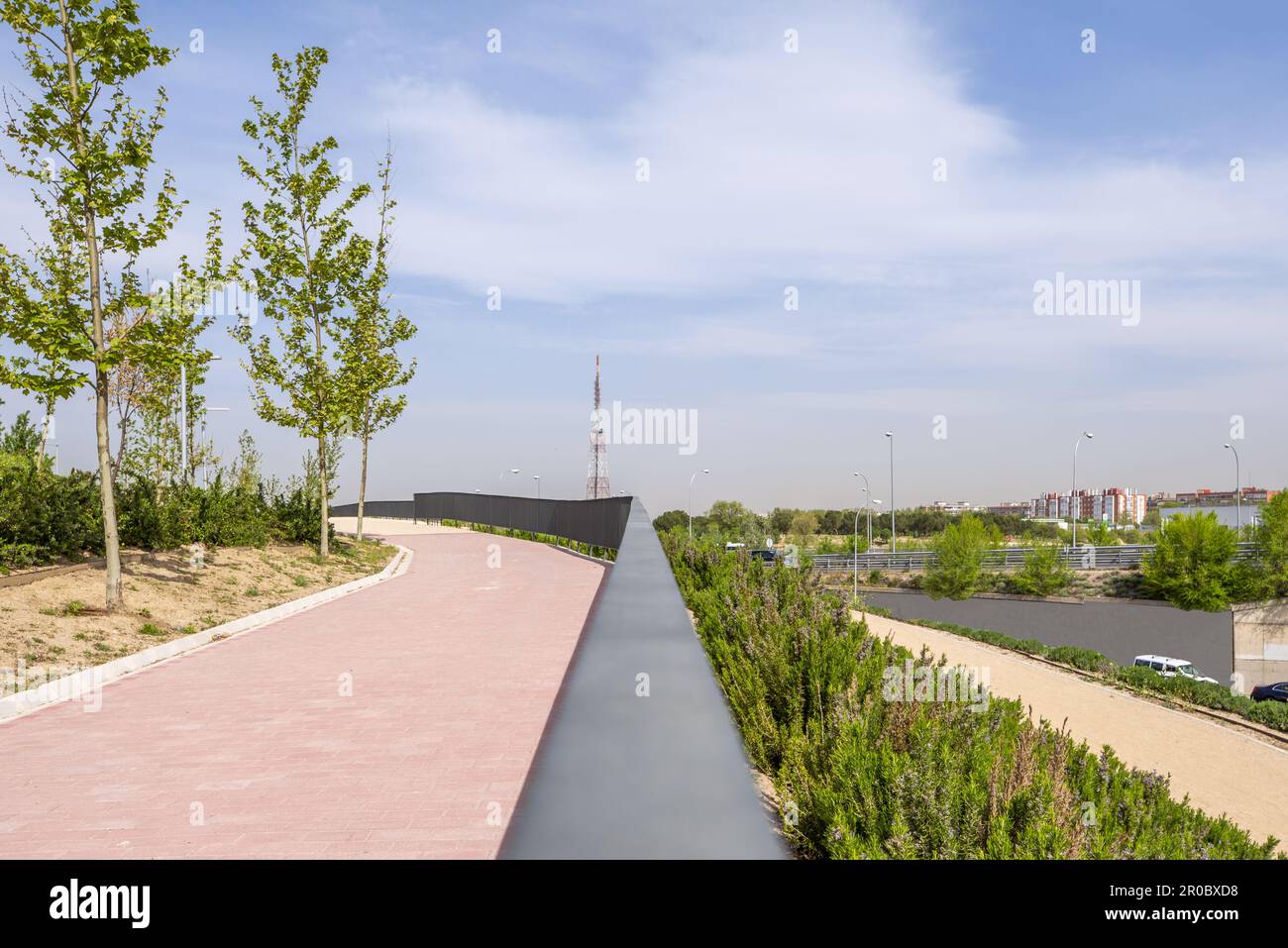 Un passaggio pedonale con pavimento in mattoni rossi e ringhiera in metallo in un nuovo parco urbano Foto Stock