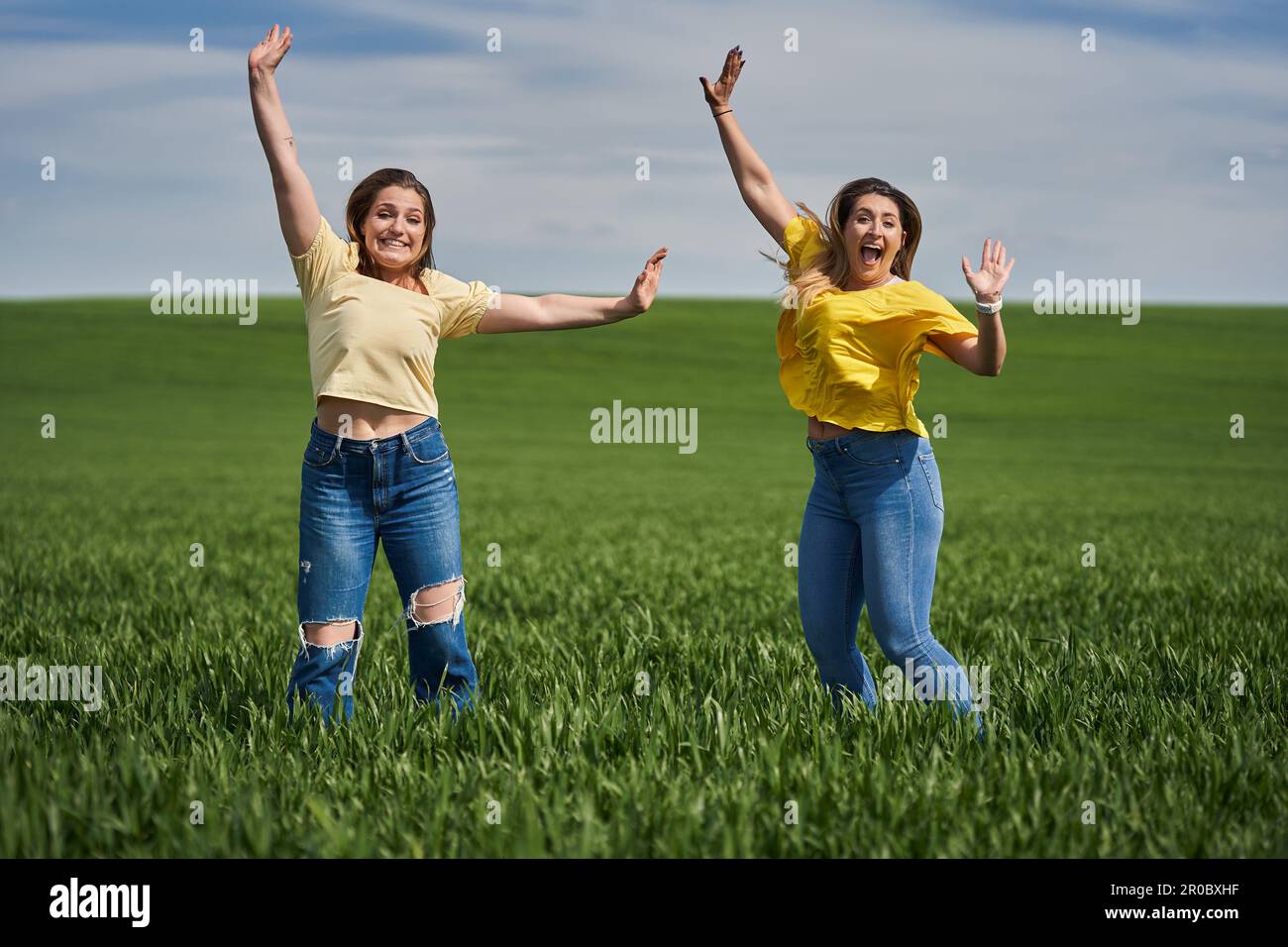 Due ragazze più grandi che saltano per la gioia ed avere divertimento in un campo di grano Foto Stock